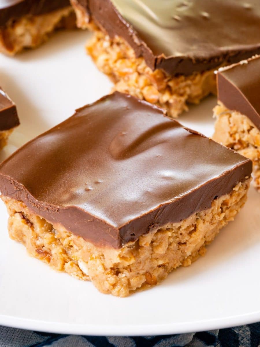 Angled view of a single peanut butter pretzel bar on white plate with thick chocolate topping - Hostess At Heart