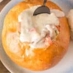 A spoon dipped into a bread bowl filled with homemade easy clam chowder. Hostess At Heart
