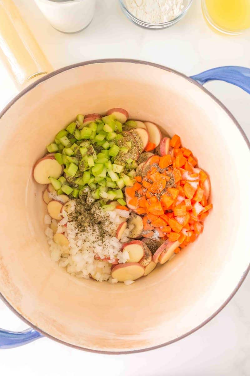 Dutch oven filled with diced onion, carrots, and celery, sliced potatoes, and dried basil, oregano, and thyme, salt and pepper - Hostess At Heart