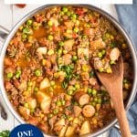 Top down view of a skillet of simmering cowboy stew filled with ground beef, sausage, potatoes, corn, peas, and beans in a tomato-based broth - Hostess At Heart