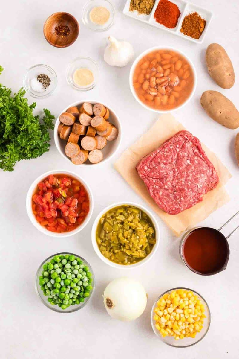 Ingredients for cowboy stew arranged on counter including ground beef, sausage, potatoes, canned beans, tomatoes, corn, and spices - Hostess At Heart
