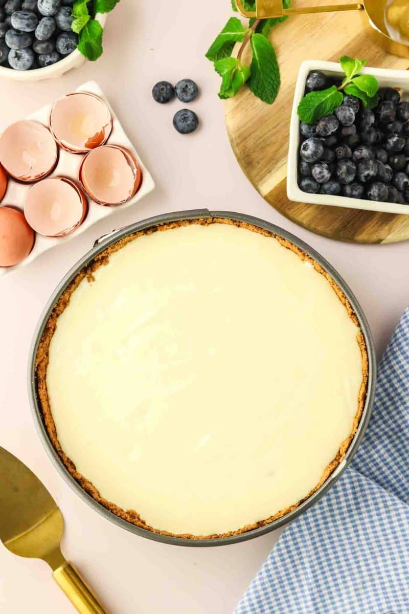 Smooth blueberry cheesecake batter poured over graham cracker crust in springform pan before baking - Hostess At Heart