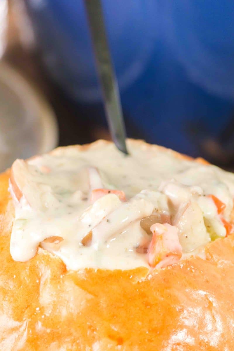 Sideview of a bread bowl overflowing with creamy clam chowder recipe made with green chilies - Hostess At Heart
