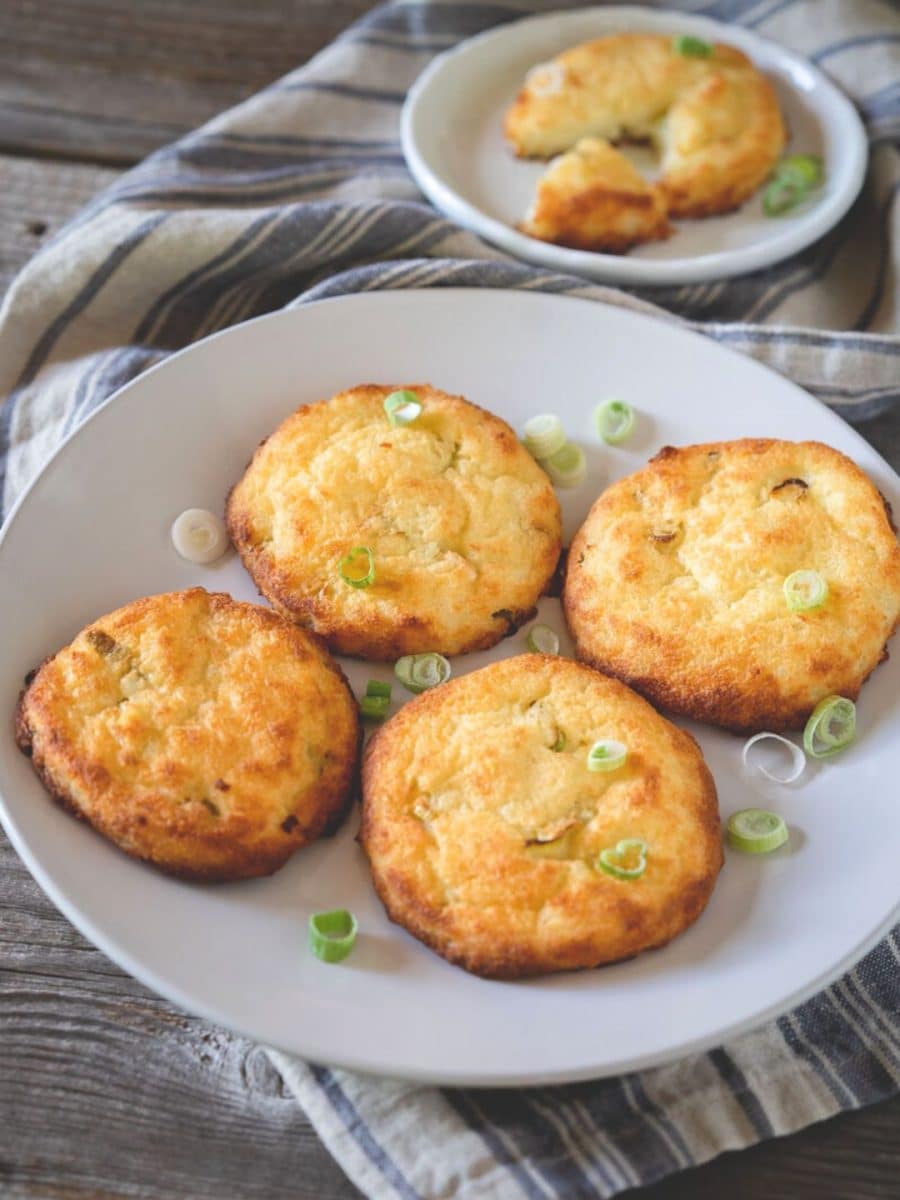 A plate holding 4 crispy potato cakes garnished with sliced green onions - Hostess At Heart