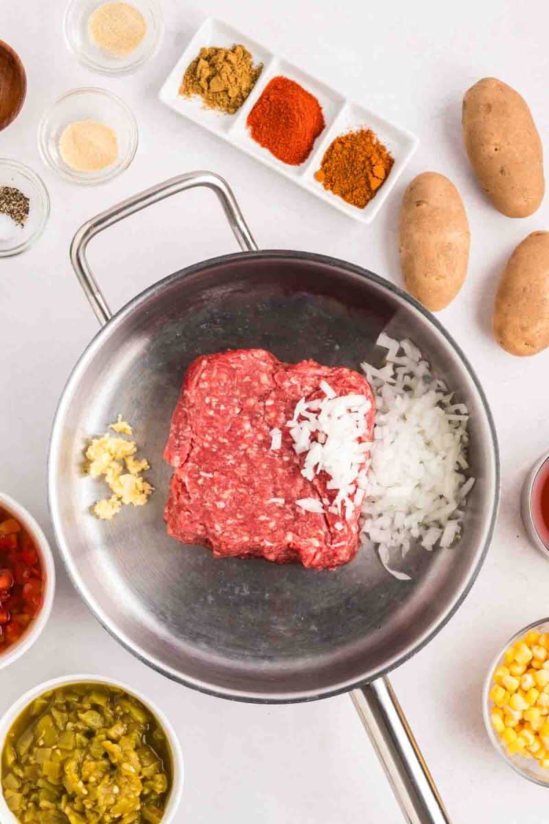 Raw ground beef, diced onion and mined garlic in a skillet preparing to be browned together. Hostess At Heart