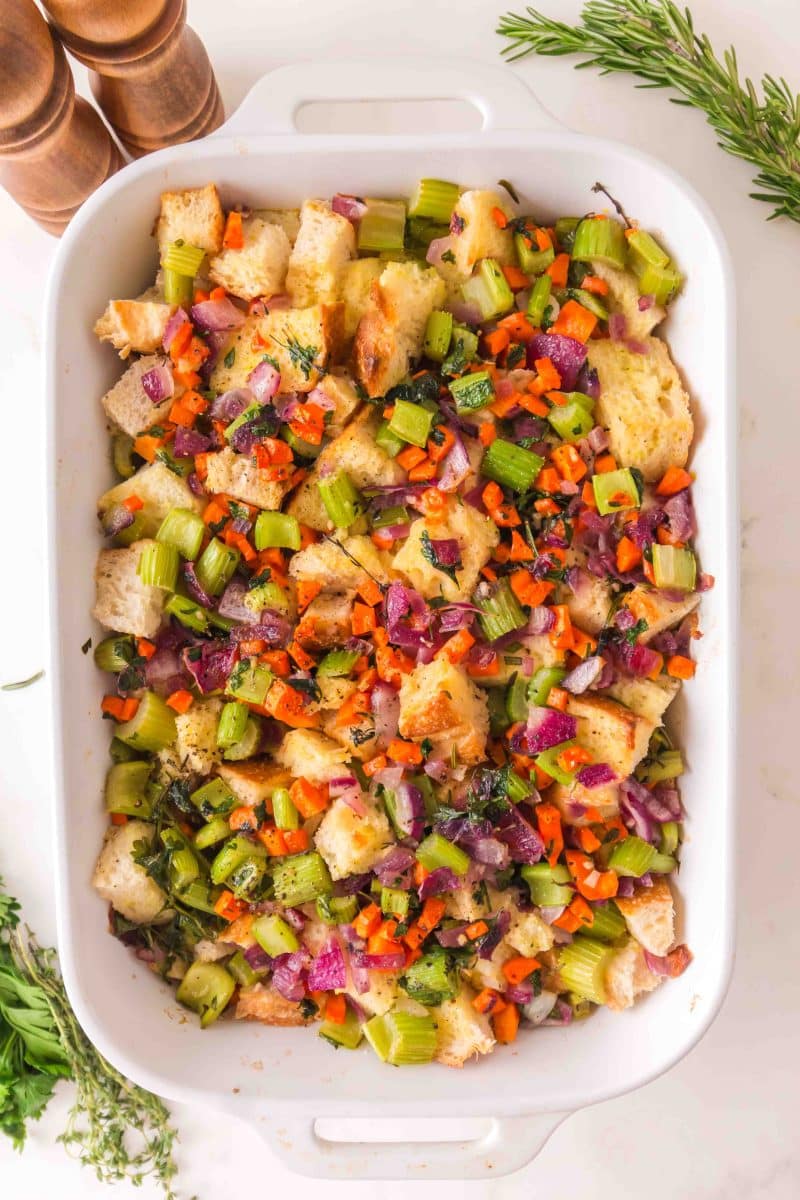Top down view of a baking dish fresh from the oven filled with golden brown sourdough stuffing in a white baking dish with crispy edges and fresh herbs - Hostess At Heart