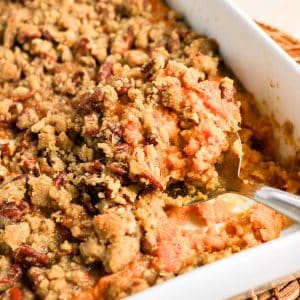 Serving spoon scooping a portion of sweet potato casserole with pecan topping - Hostess At Heart