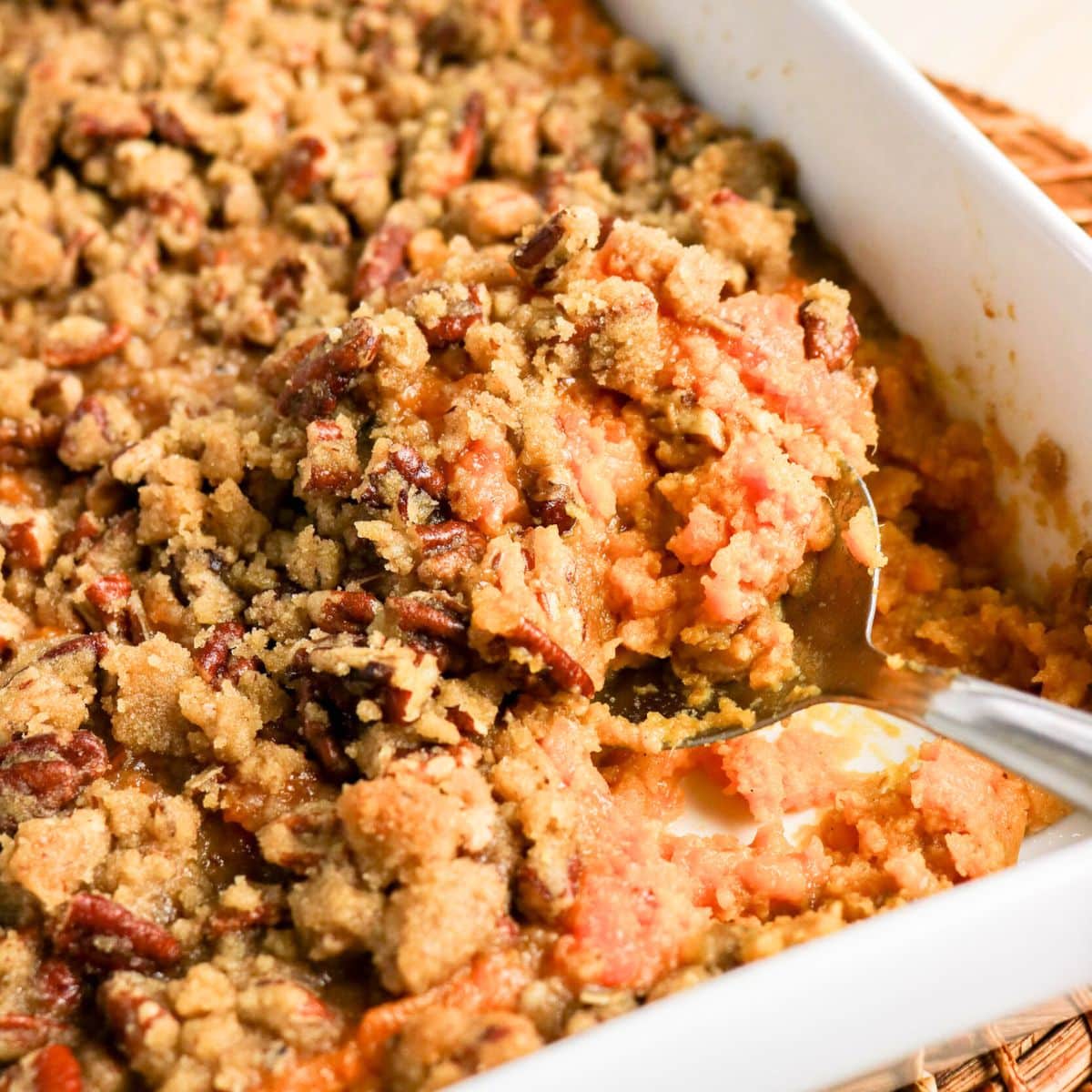 Serving spoon scooping a portion of sweet potato casserole with pecan topping - Hostess At Heart