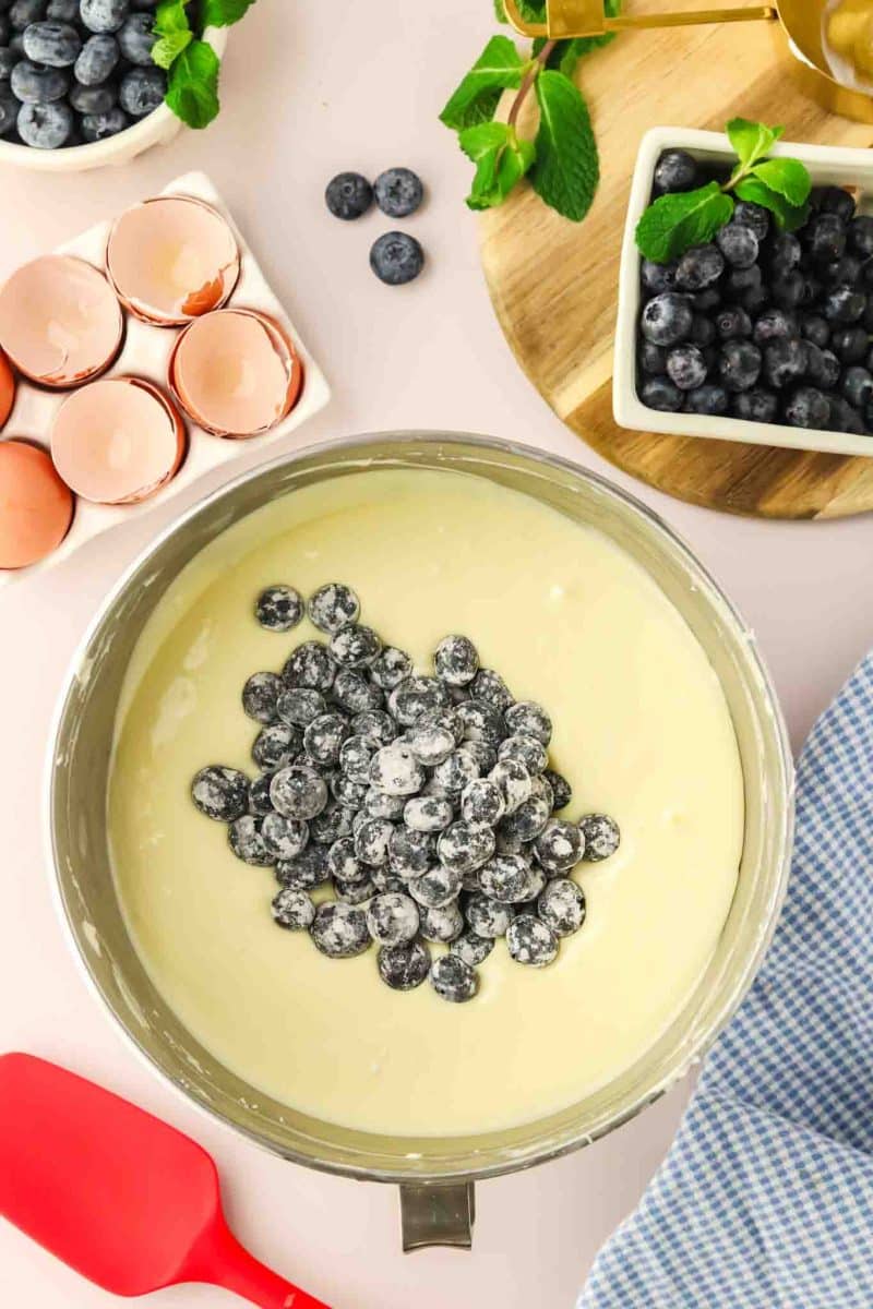 Flour crusted fresh blueberries in a bowl of smooth blueberry cheesecake batter - Hostess At Heart