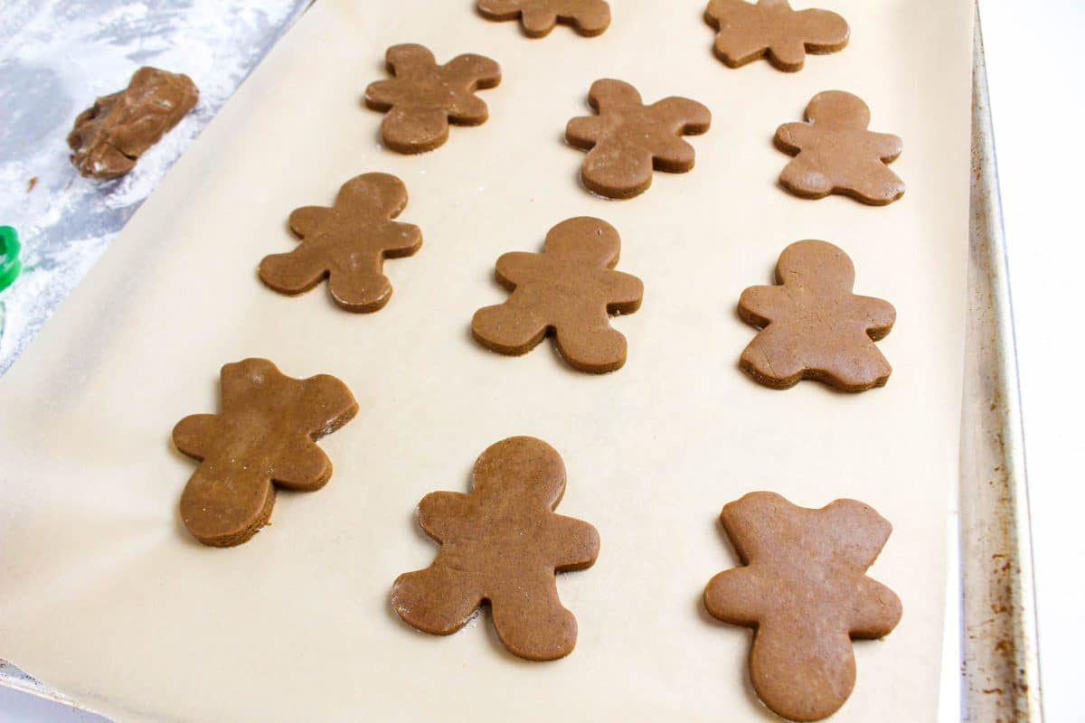 Gingerbread cookie dough cut out into gingerbread men and reindeers and placed on a parchment paper lined baking sheet- Hostess At Heart