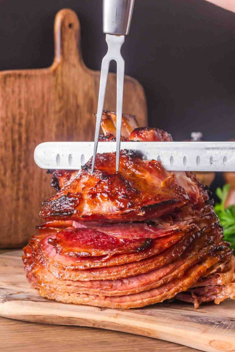 Whole honey baked ham on wooden cutting board ready to slice showing caramelized exterior - Hostess At Heart