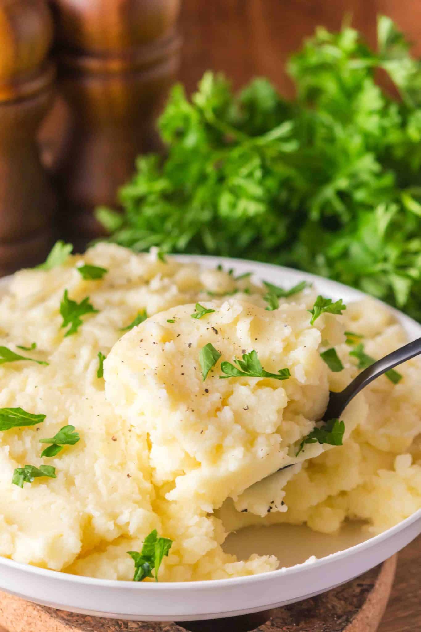Serving spoon lifting a scoop of creamy Yukon Gold mashed potatoes from a bowl - Hostess At Heart