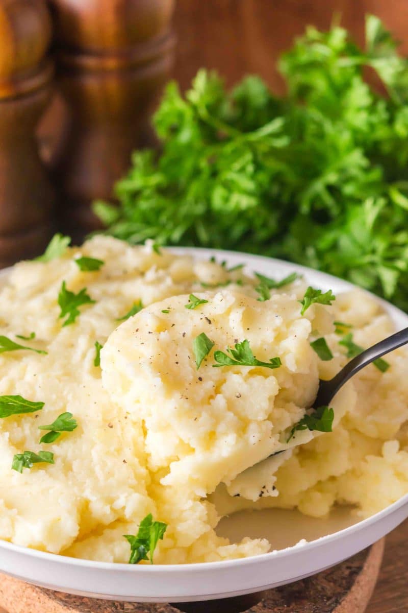 Serving spoon lifting a scoop of creamy Yukon Gold mashed potatoes from a bowl - Hostess At Heart