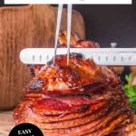 An image for Pinterest of a whole honey baked ham on wooden cutting board ready to slice showing caramelized exterior - Hostess At Heart