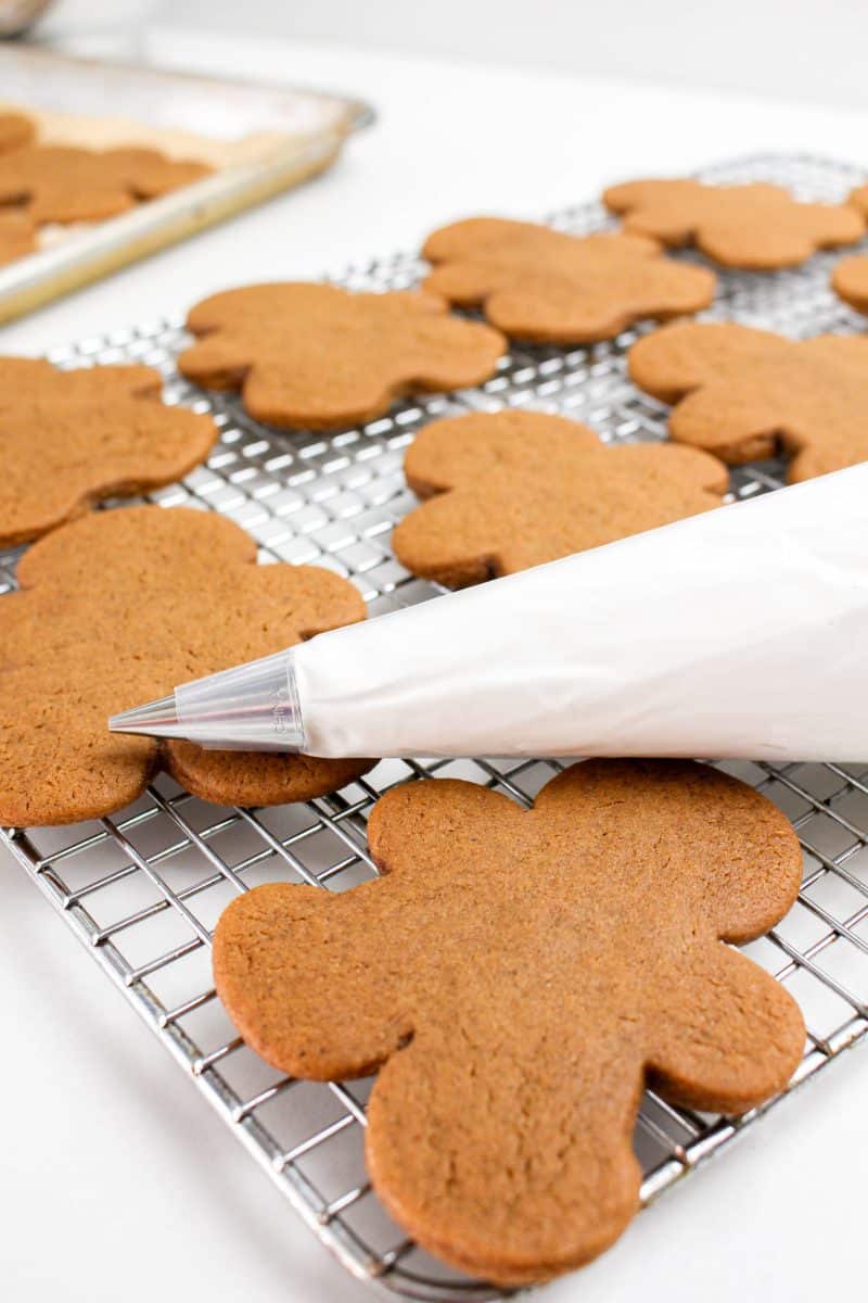 Baked gingerbread men on a cooling rack with a piping bag filled with royal icing - Hostess At Heart