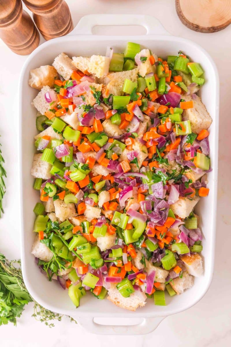 Raw sourdough stuffing mixture with vegetables, eggs, and chicken broth in baking dish - Hostess At Heart
