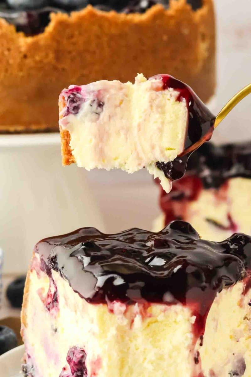 Creamy bite of blueberry cheesecake on a fork showing graham cracker crust and blueberry-studded filling - Hostess At Heart