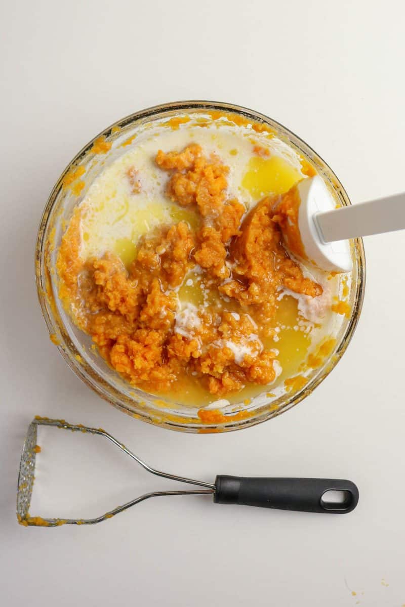 Creamy sweet potato casserole filling mixed with eggs, butter, and cinnamon in a bowl with an immersion blender- Hostess At Heart