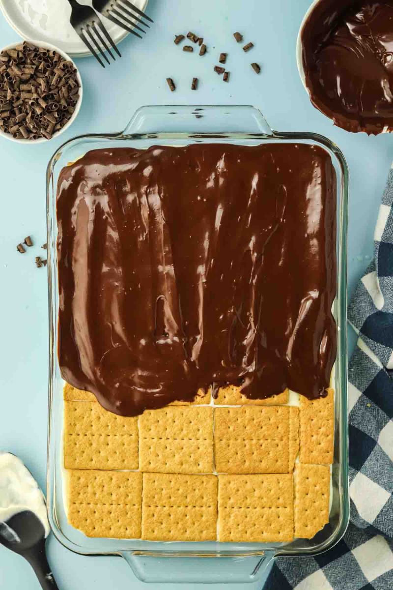 Pouring warm chocolate frosting over top layer of graham crackers - Hostess At Heart