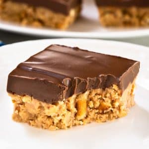 Single peanut butter pretzel bar on white plate with chocolate topping with a bite taken out of it - Hostess At Heart