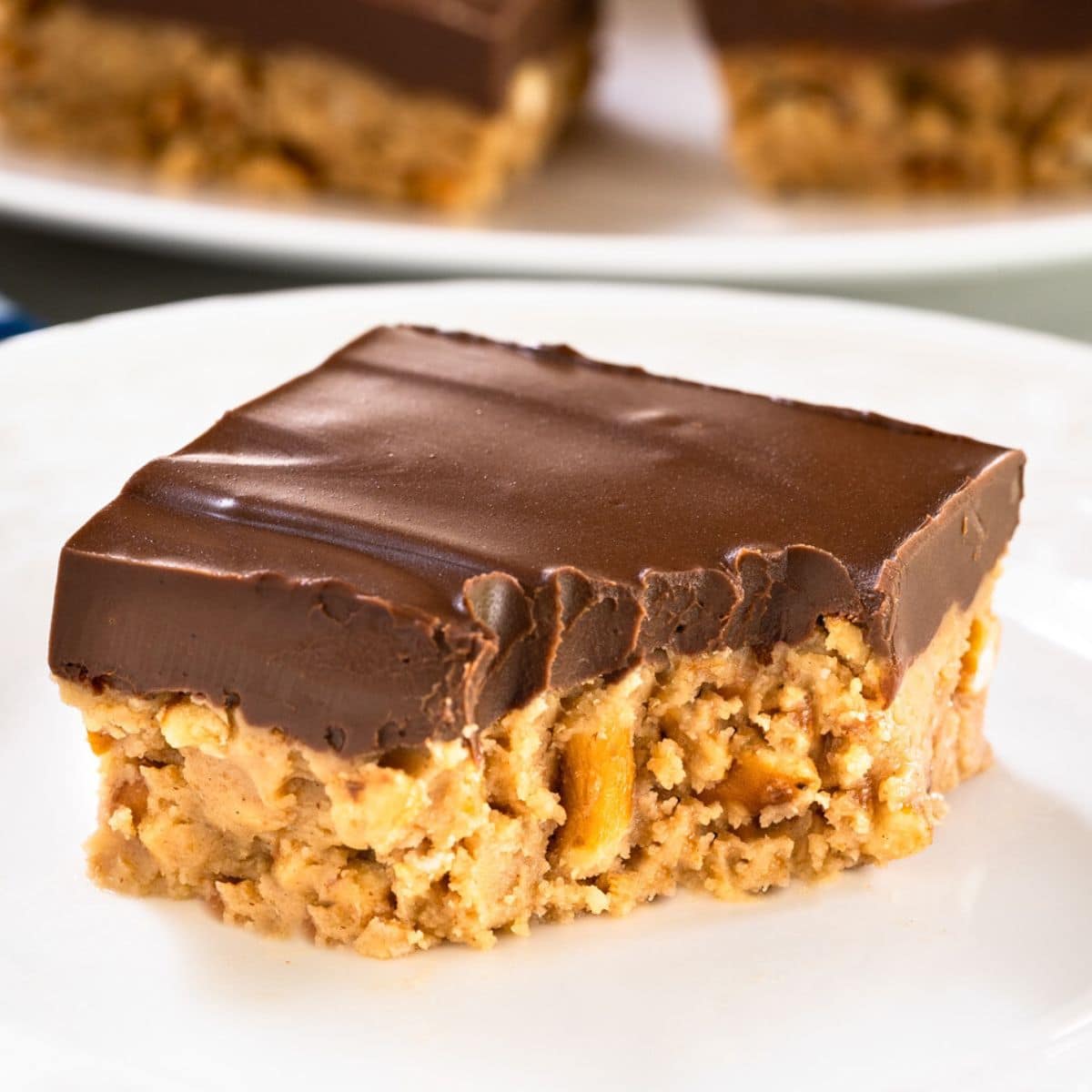Single peanut butter pretzel bar on white plate with chocolate topping with a bite taken out of it - Hostess At Heart
