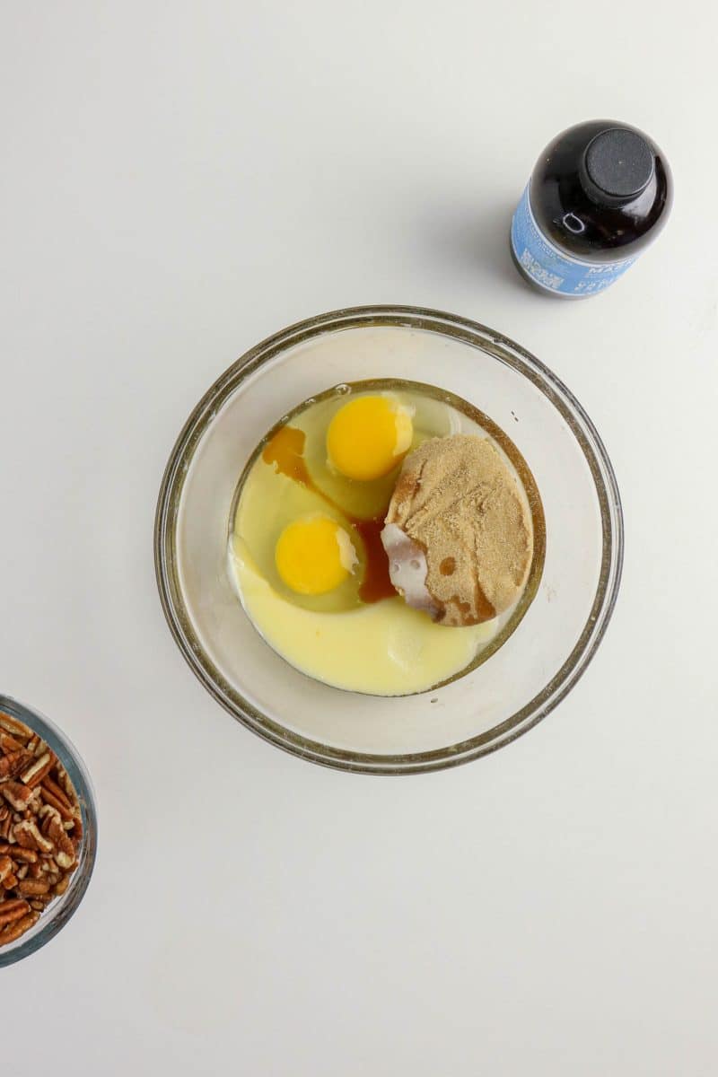 A mixing bowl filled with the sweet filling ingredients necessary to make pecan topping: Brown sugar, butter, eggs, and vanilla - Hostess At Heart