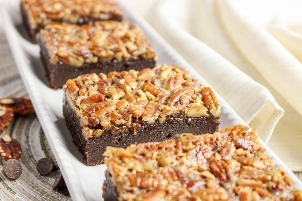 A row of pecan pie brownies showing consistent golden pecan topping on each square on a serving dish - Hostess At Heart