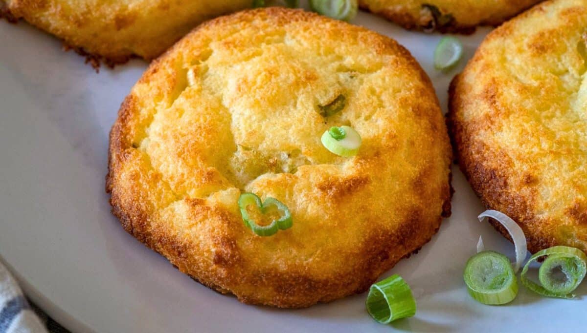 Close up view of golden brown potato cakes on a plate and garnished with sliced green onions - Hostess At Heart