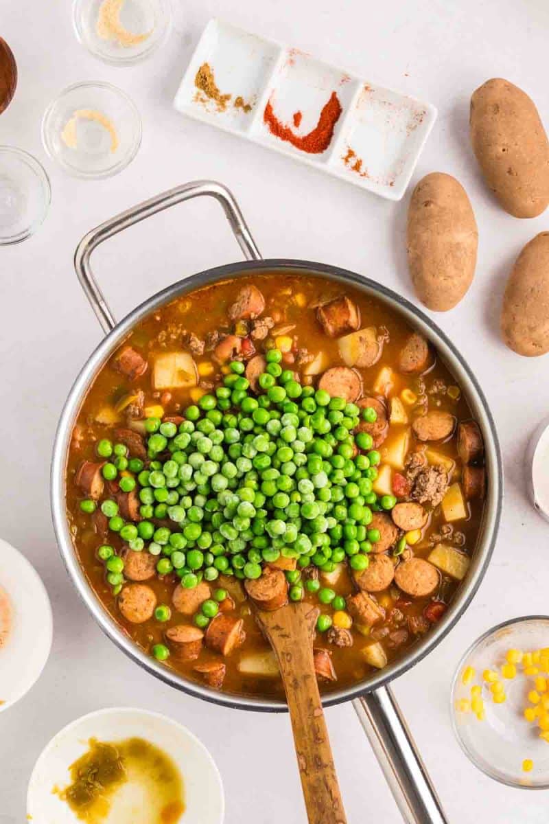 Adding frozen peas to nearly finished cowboy stew in a large skillet - Hostess At Heart