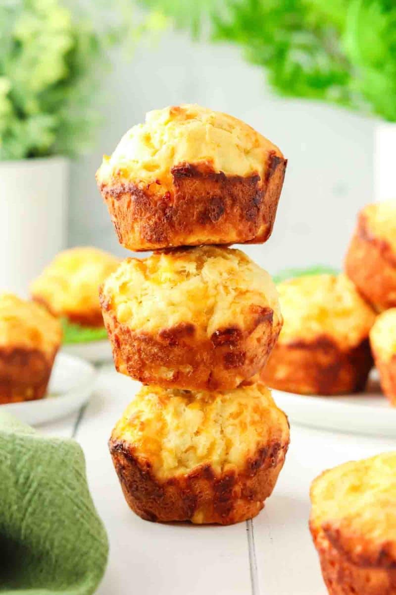 Three golden brown cheddar cheese muffins stacked on top of each other - Hostess At Heart