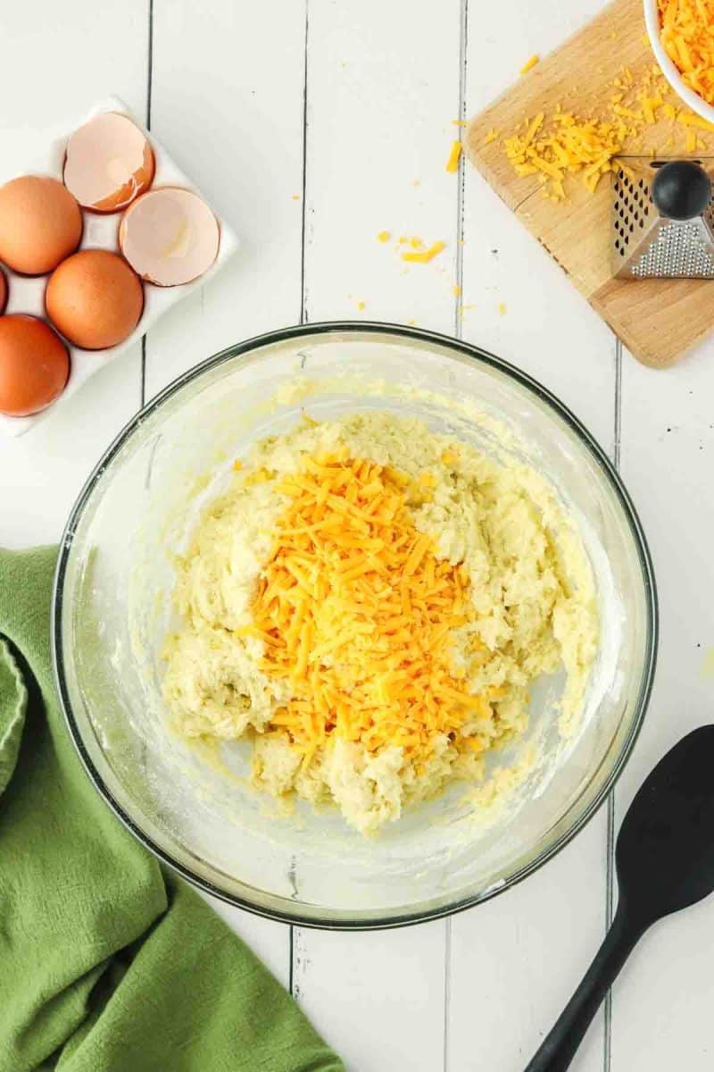 A mixing bowl filled with cheese muffin batter topped with shredded cheddar - Hostess At Heart
