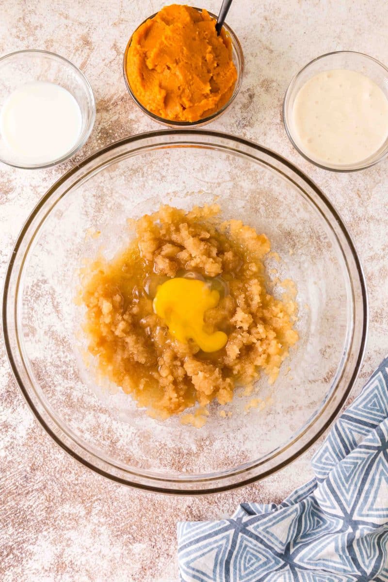 An egg added to a bowl containing mixed white sugar, brown sugar and melted butter - Hostess At Heart