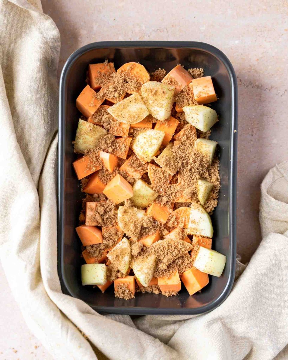 A casserole dish filled with chunks of sweet potatoes and apples with a brown sugar spice sprinkled over the top - Hostess At Heart