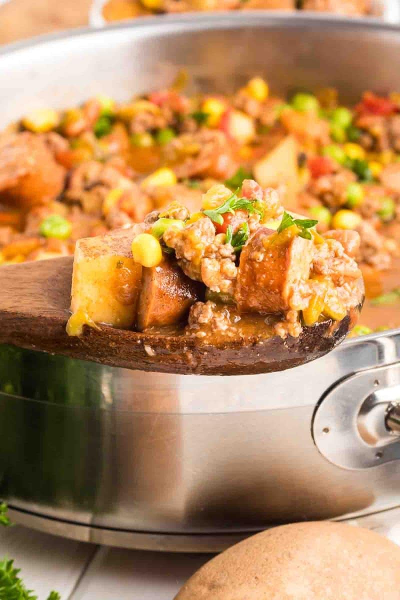 A wooden spoon filled with Cowboy stew in a pot showing tender potatoes and vegetables in rich broth - Hostess At Heart