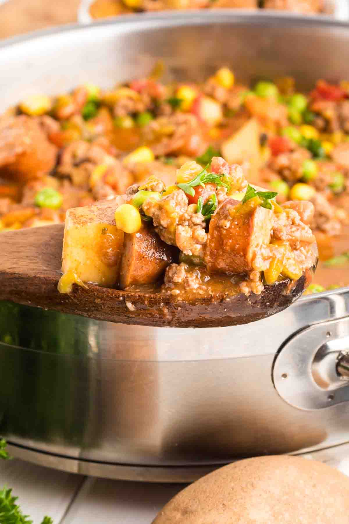 A wooden spoon filled with Cowboy stew in a pot showing tender potatoes and vegetables in rich broth - Hostess At Heart