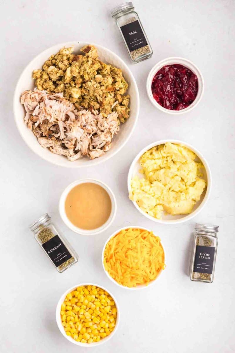 Ingredients for Thanksgiving Leftover Casserole including shredded turkey, mashed potatoes, gravy, stuffing, corn, shredded cheese, spices, and cranberry sauce