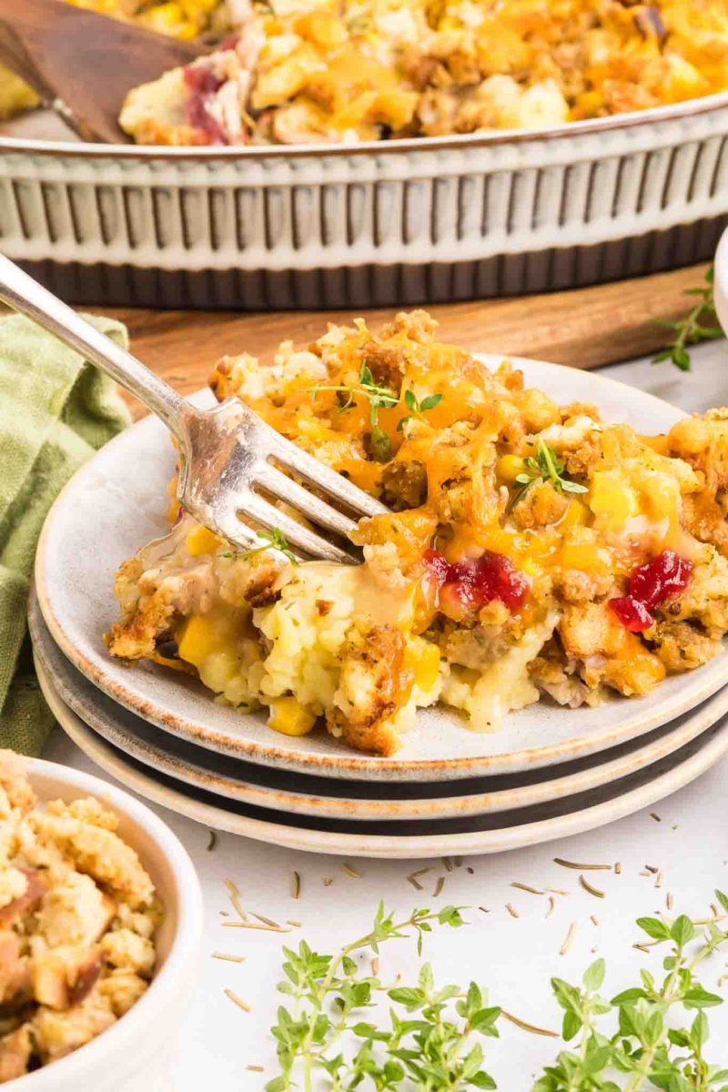 A fork stuck into a slice of Thanksgiving Leftover Casserole on a white plate showing all the delicious layers - Hostess At Heart