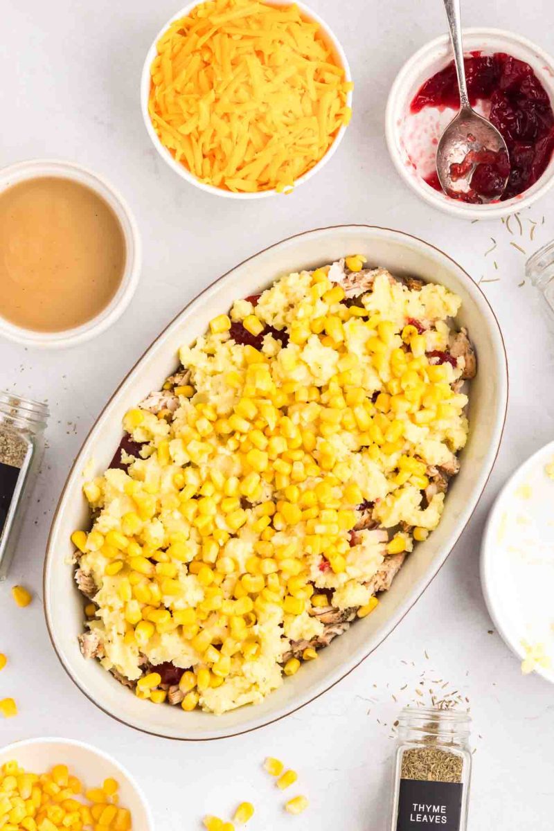 Corn sprinkled over creamy mashed potatoes layered over turkey and cranberry sauce in baking dish - Hostess At Heart