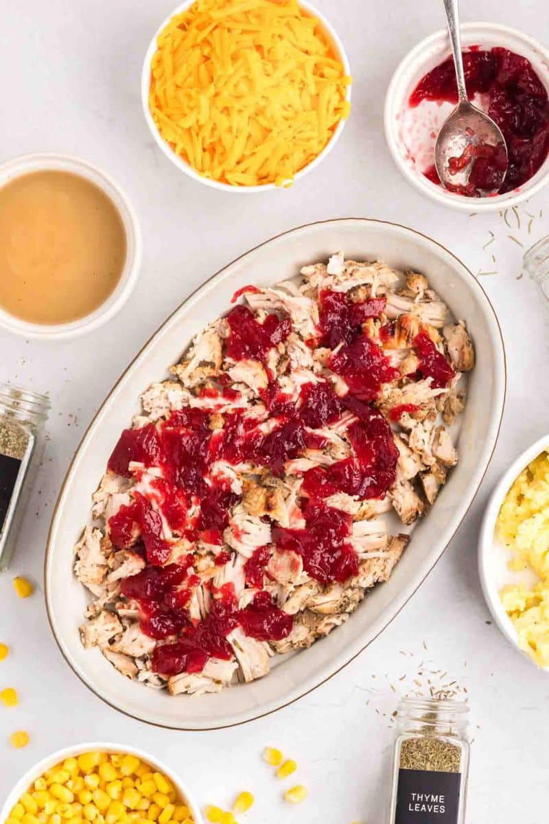 Cranberry sauce dolloped over turkey in casserole dish - Hostess At Heart