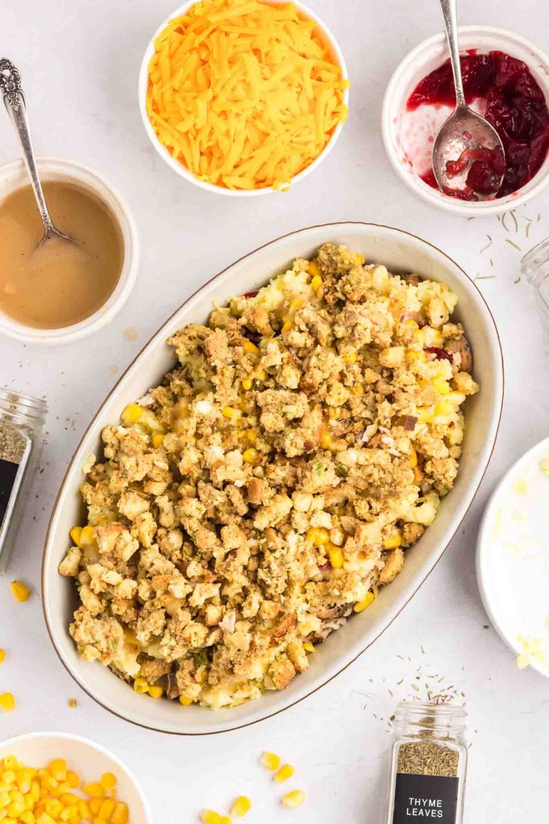Stuffing layered over creamy mashed potatoes, turkey, and cranberry sauce in baking dish - Hostess At Heart