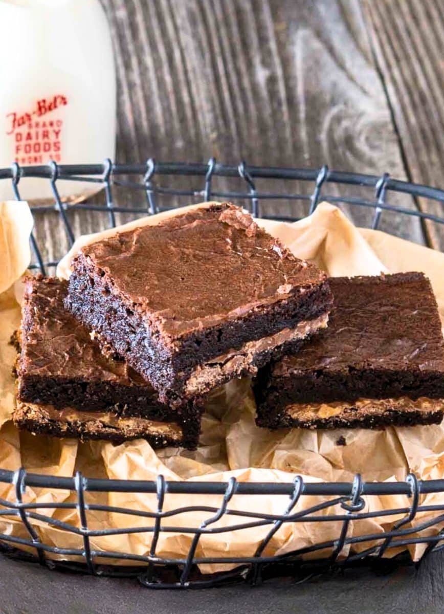 Close-up view of three chocolate toffee brownies with heath candy bars baked into the center sitting in a parchment-paper lined basket. Hostess At Heart