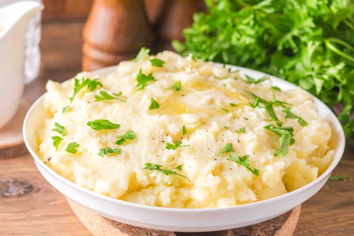 Creamy Yukon Gold mashed potatoes in a white serving bowl with melted butter and chopped parsley on top - Hostess At Heart