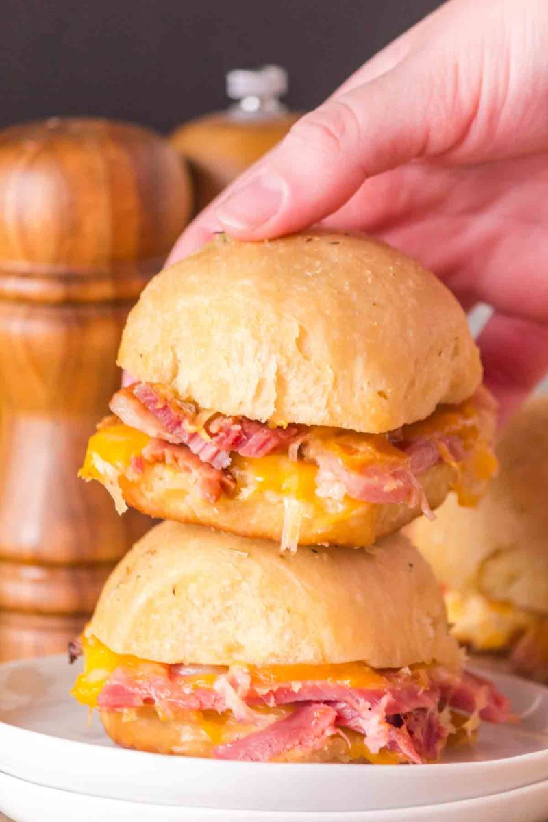 Sideview of a hand holding a Hawaiian ham and cheese slider with stretchy melted cheese. Hostess At Heart