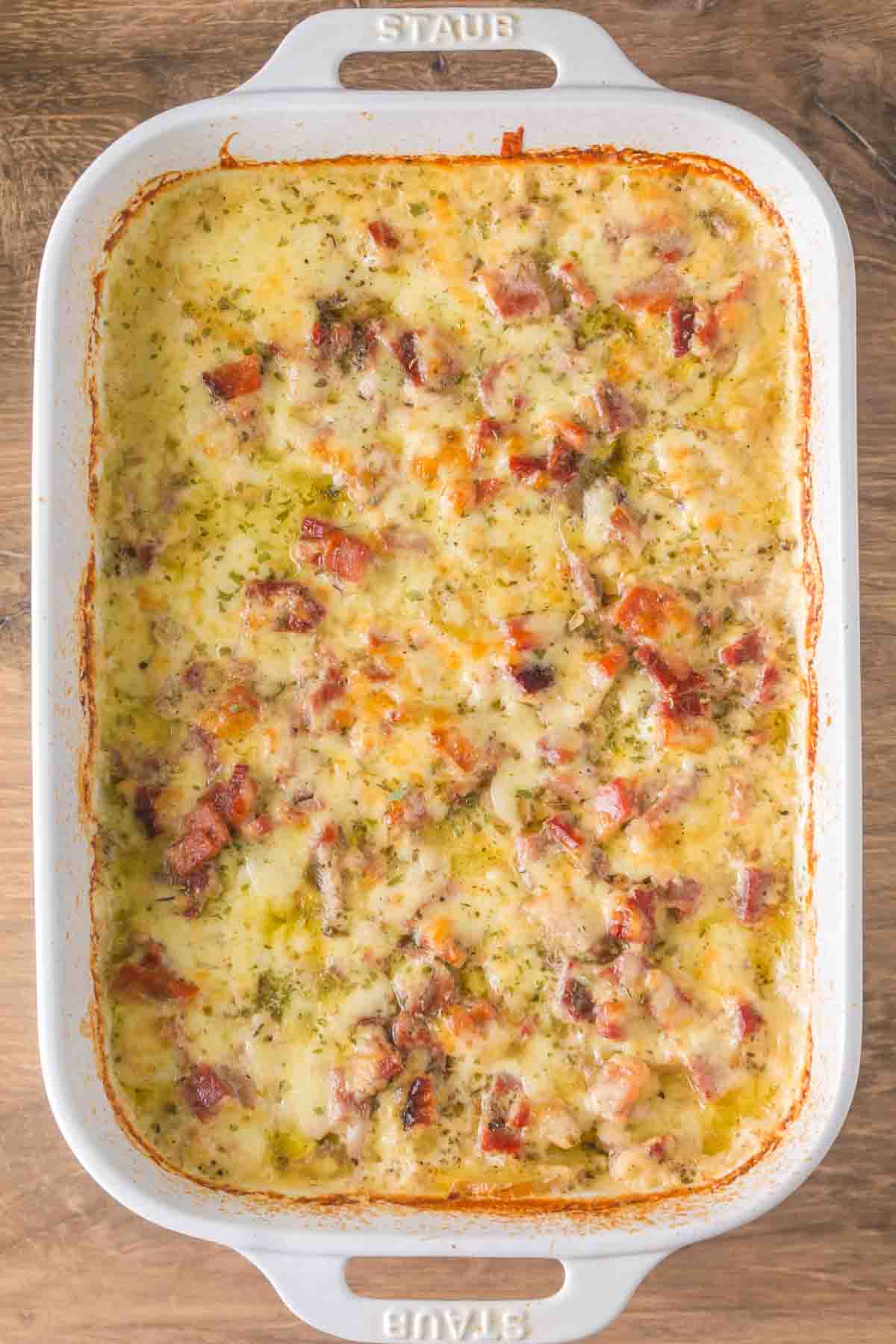 Golden brown scalloped potatoes with ham in white baking dish showing creamy layers and melted cheese top - Hostess At Heart