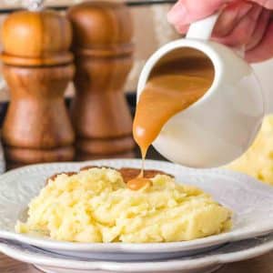 Pouring hot beef broth gravy from a white gravy boat showing smooth texture - Hostess At Heart