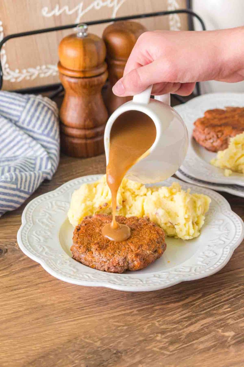 Pouring hot beef broth gravy over a beef patty - Hostess At Heart