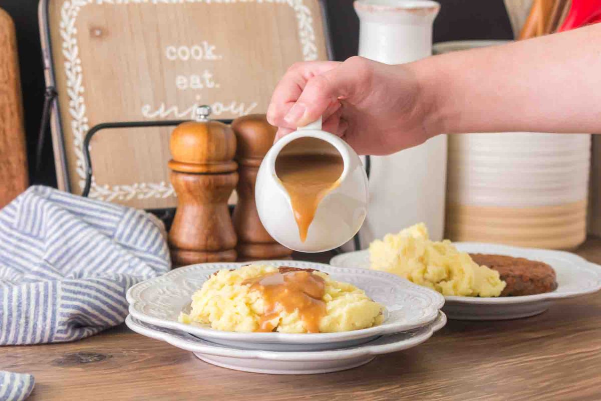 Smooth beef gravy in white gravy boat poured over creamy mashed potatoes - Hostess At Heart