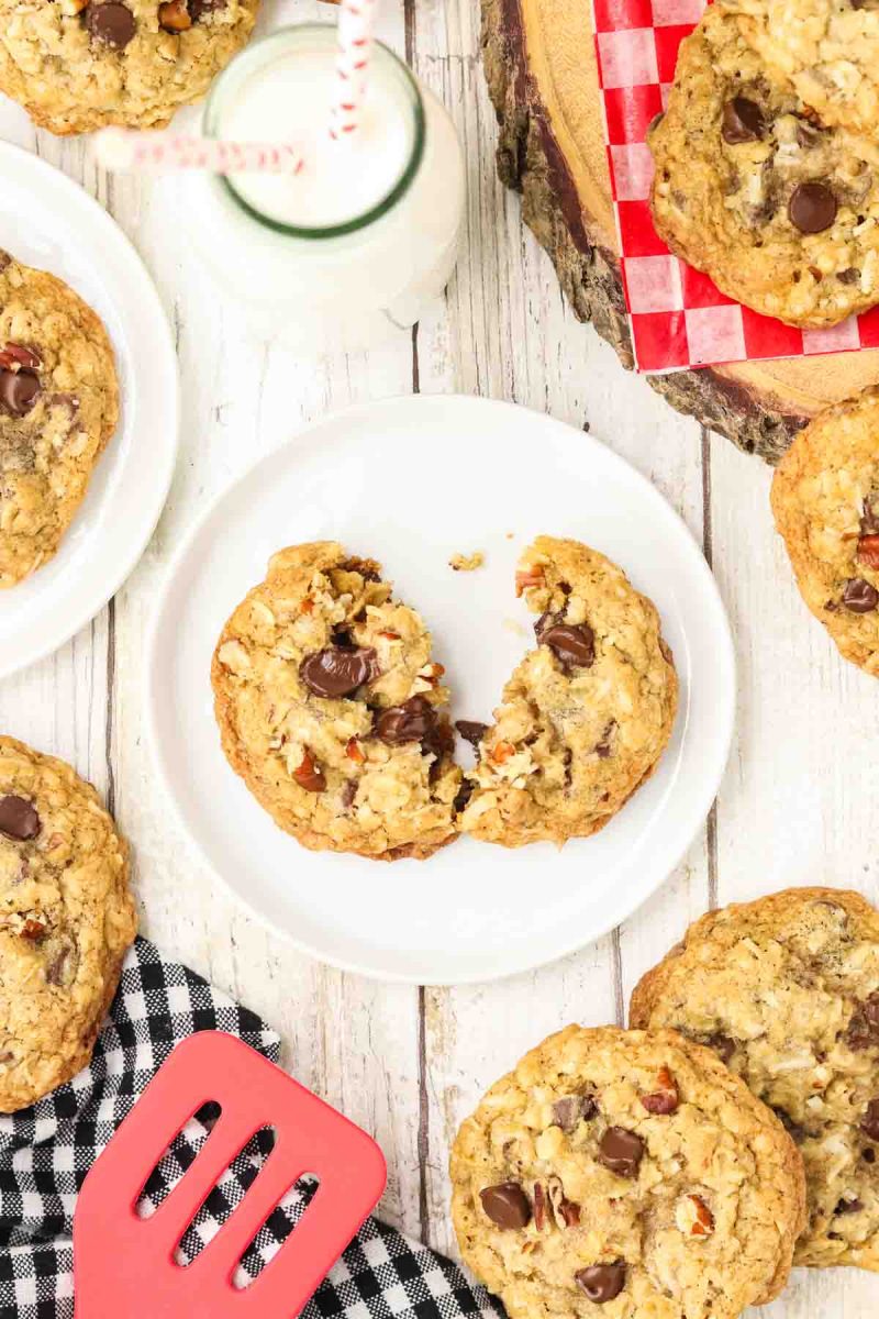 Cowboy cookie broken in half on white plate revealing chewy interior texture packed with gooey chocolate chips, coconut, pecans and oats, showing contrast between crispy golden edges and soft center - Hostess At Heart