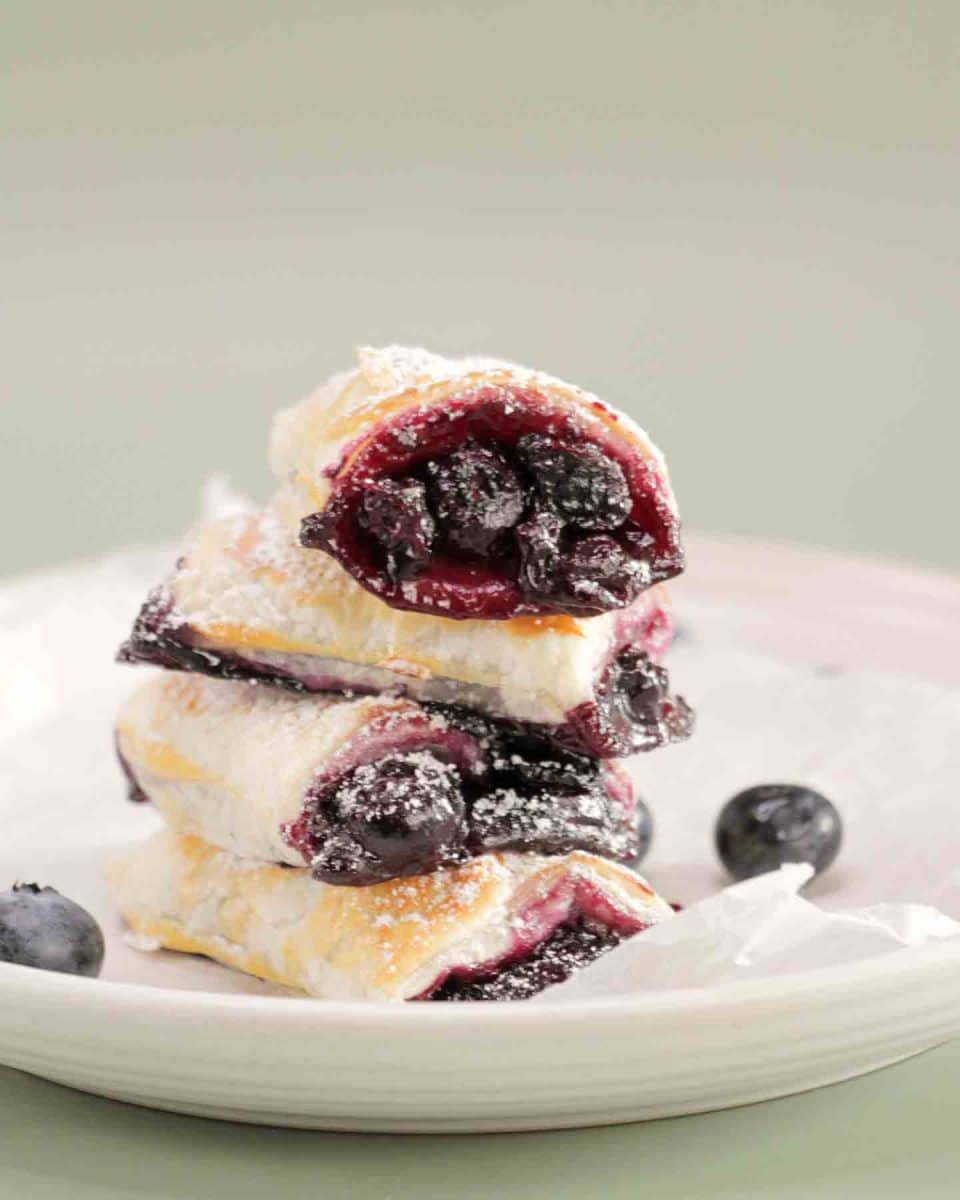 Front view of a stack of 3 puff pastry rolls filled with blueberries and dusted with powdered sugar