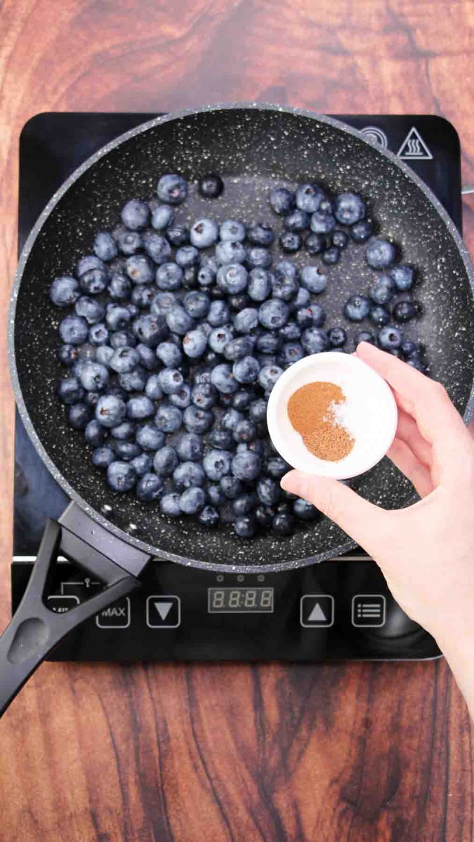 A skillet filled with fresh blueberries being seasoned with cinnamon, nutmeg, and salt - Hostess At Heart